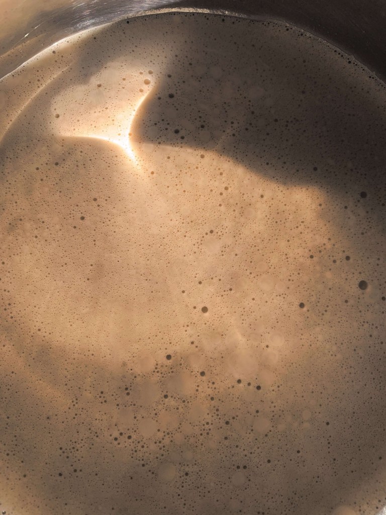 Close up photo of coffee in a pot witg the aunlight reflecting on it. The light has formed the shape of a heart.