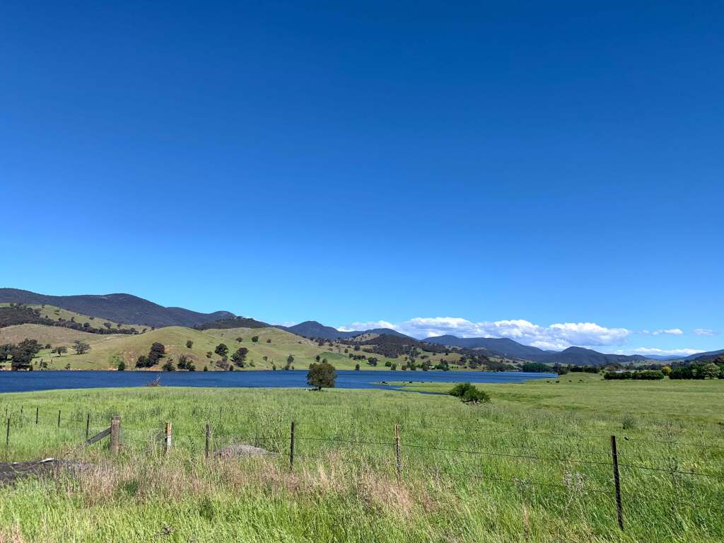 photo of a fenced off lush valley with a lake in the middle and blue skies