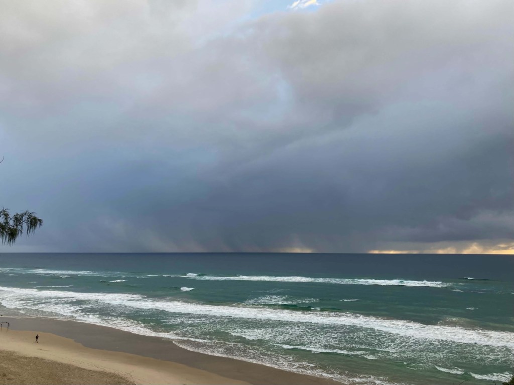 Photo of the sun, behind a band of grey clouds, its colours mildly visible. 