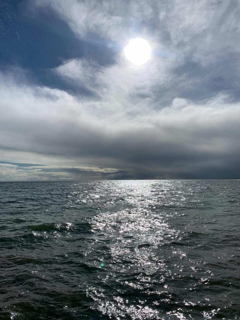 Photo of the sun reflecting on the ocean, creating a glinting surface.