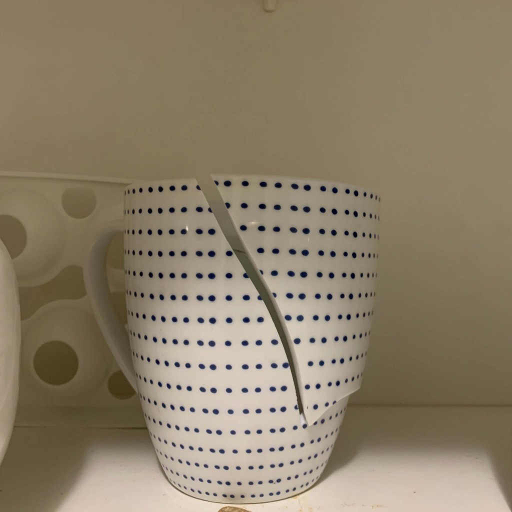 Close up photo of a mug with a large vertical crack on it. 