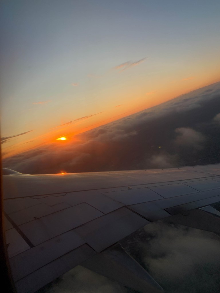 Photo of the sunset in the horizon, as seen from the window seat of a plane that’s making a sharp turn. 