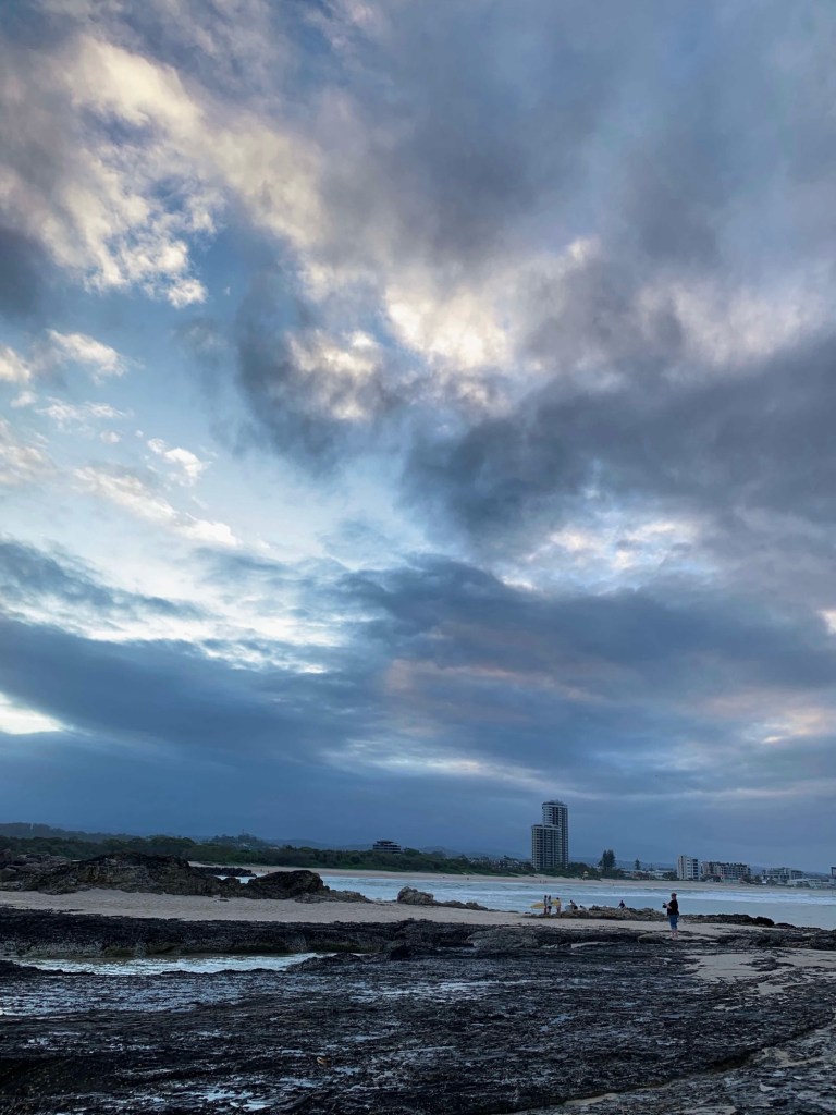 Photo of Currumbin beach in the Gold Coast, taken from the rocks at dusk with dark and stormy clouds gathering in the distant horizon. 