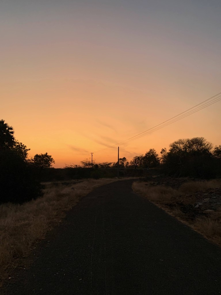 Photo of the sunset’s colours in the horizon and a road leading towards it. 