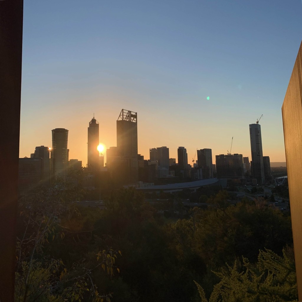 Photo of the sun rising from behind the Rio Tinto building (amongst others) in the Perth CBD. 