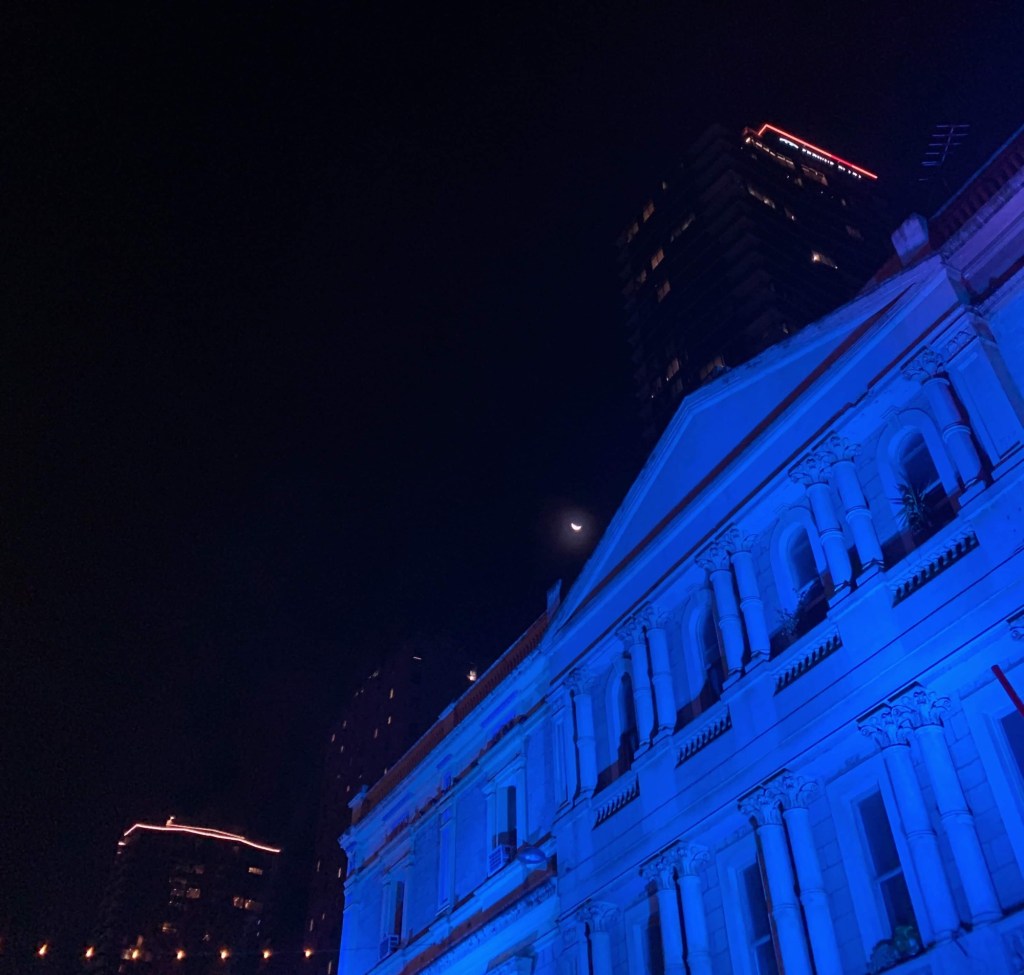 Photo of the half moon overshadowed by the lights from skyscrapers in the city. 