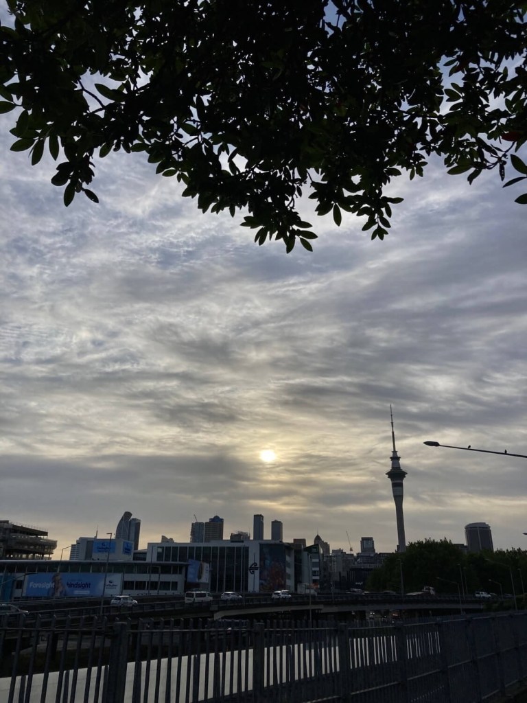 Photo of a partly cloudy morning, with the sun filtering through the clouds and the Auckland Sky City in the background. 