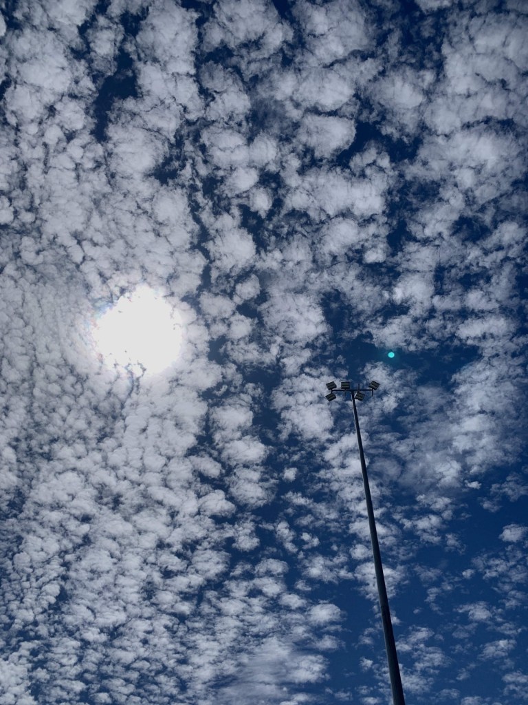 Photo of a cloudy sky, with clouds milling around the sun and blue patches in between them. 