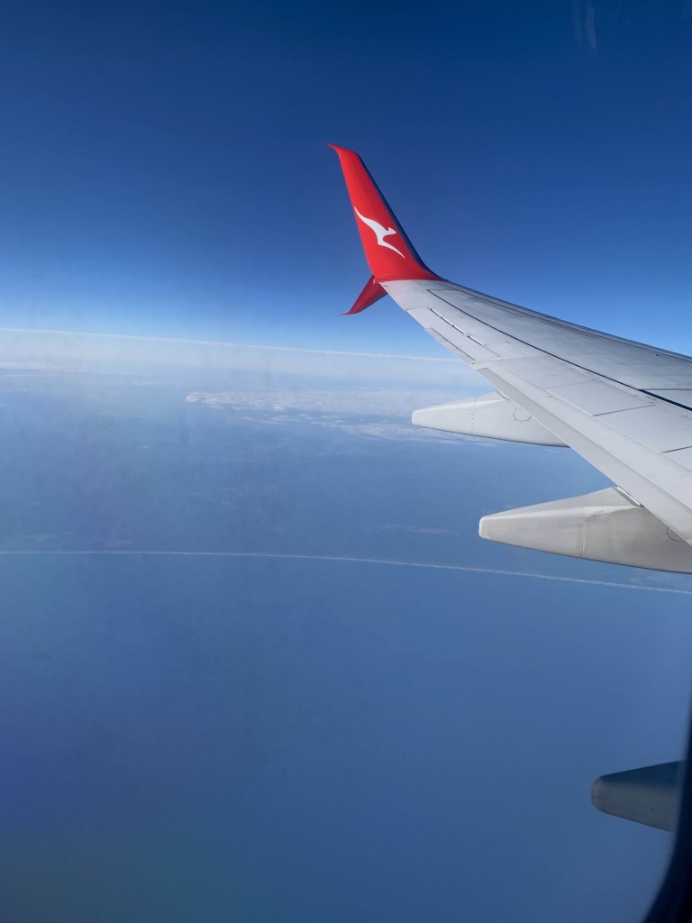 Photo of the intersection of the ocean and sky, as seen from the window of a plane. The plane’s wing is visible in the photo. 