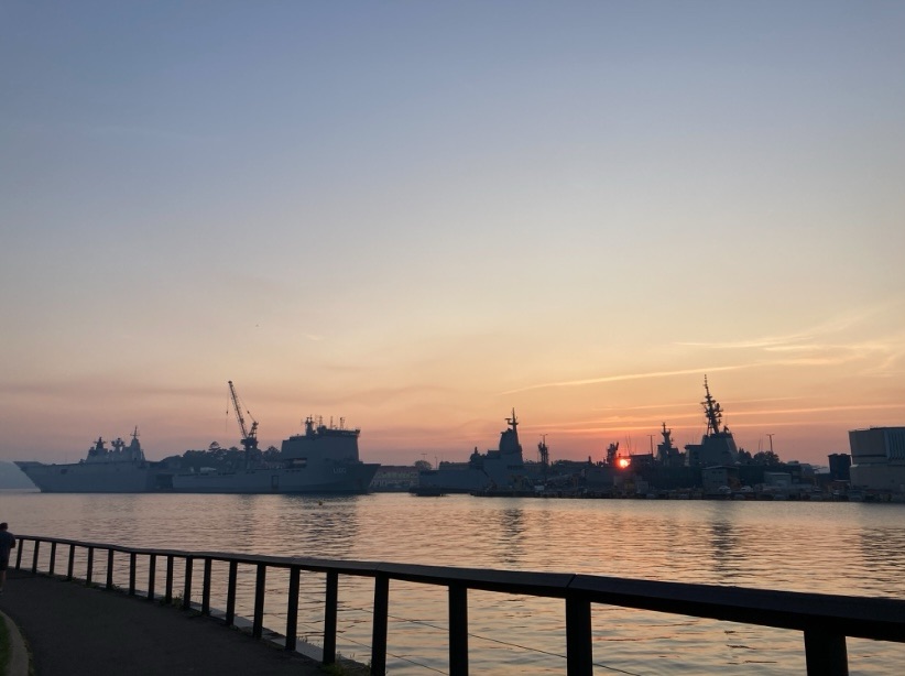 Photo of the sun rising in the background and silhouettes of big ships in the foreground, Sydney harbour. 