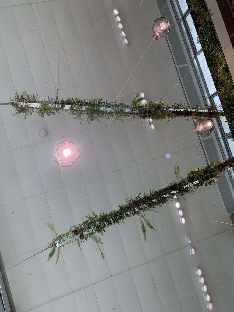photo of the ceiling at the Singapore airport, where there's plants in thin metal rods running along the ceiling and lantern lights between them