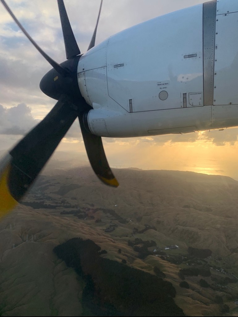 Photo of the landscape of Wellington, New Zealand, at sunset, as seen from the window of a plane. 