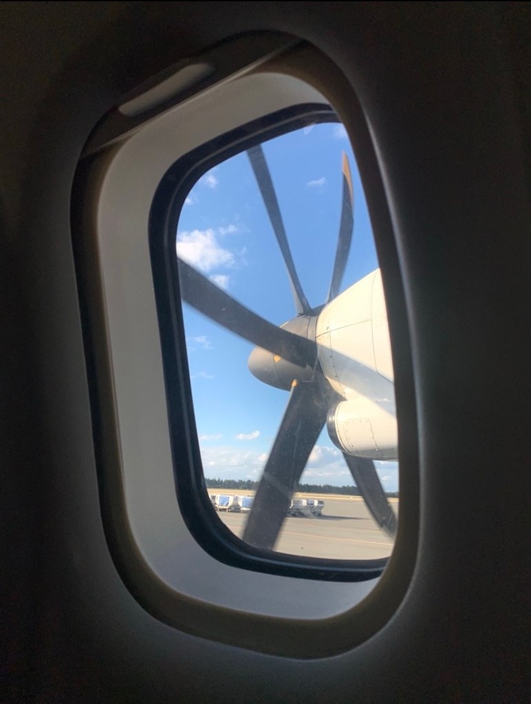 Photo of a small plane’s propellers, as seen through the window of the plane. 