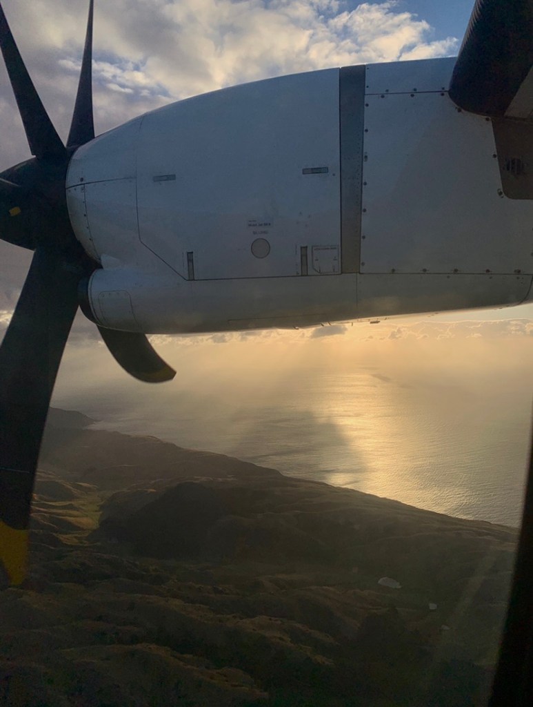 Photo of the sunset’s glow as seen from the window of the plane, with the light in halo around the plane’s engine. 