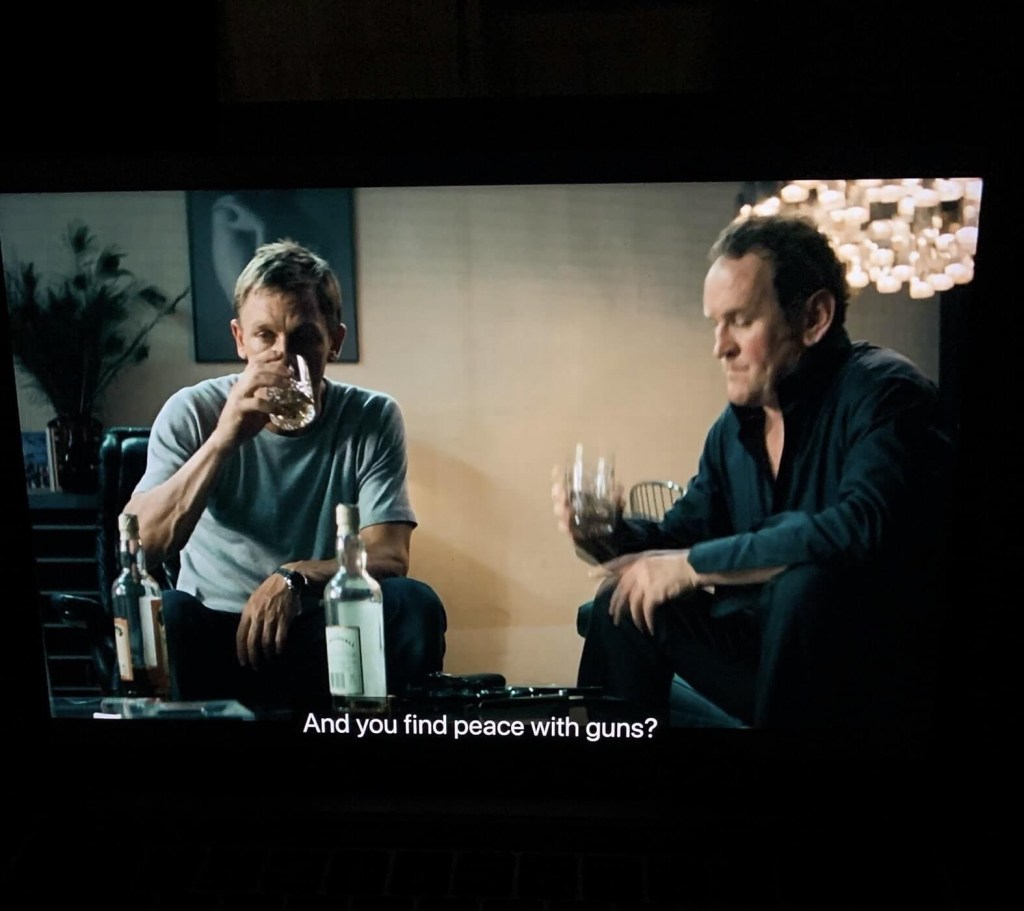 Photo of a scene from the 2004 movie, Layer cake. In the scene, Daniel Craig, as XXXX, and his friend sit drinking whisky and XXXX says, “And you find peace with guns?” as seen on the subtitles. 