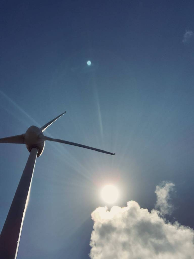 photo of the sun as seen from below with a single white cloud near it, with a large windmill visible in the image