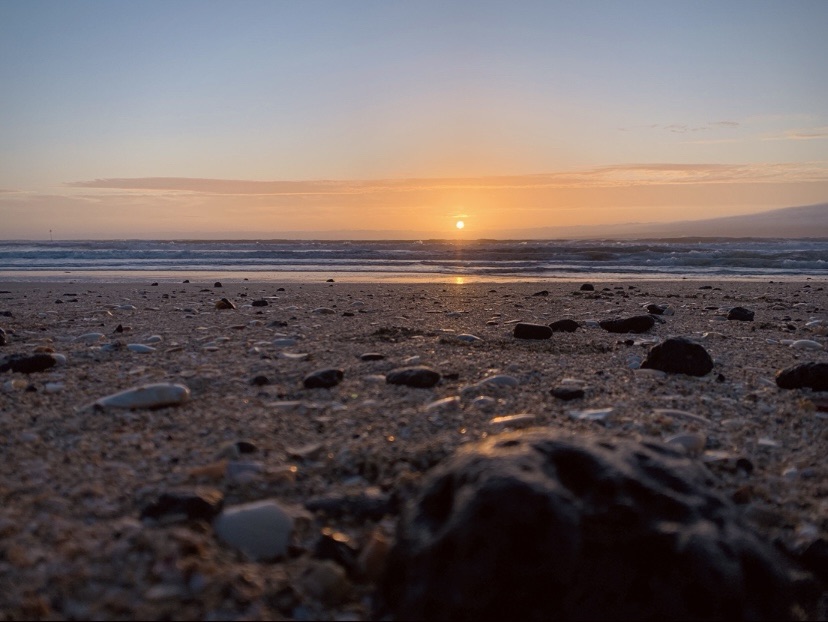 Photo of the sun rise glinting on the pebbles on a beach. 