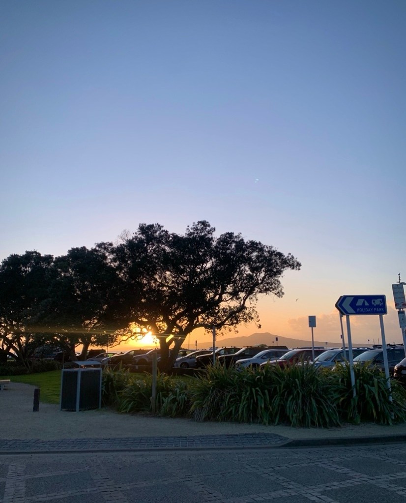 Photo of the sunrise over a busy car park by the Takapuna beach in Auckland. 