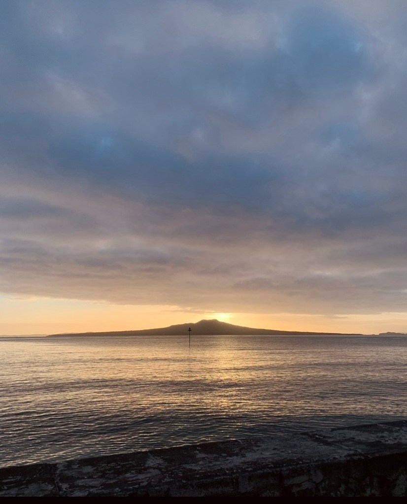 photo of the sun rising from behind Rangitoto Island as seen from Takapuna Beach in Auckland